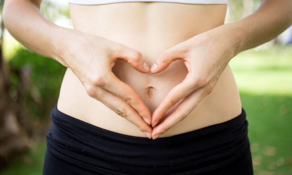 The image frames on the belly part of female in sport attires uses her hands to form a heart shape sign at her belly button