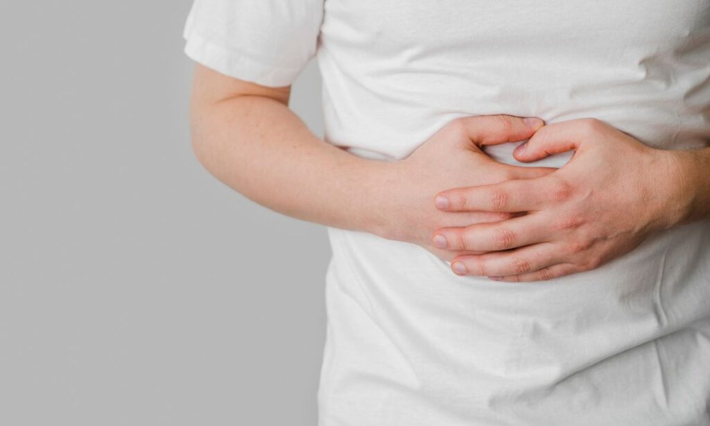 A man in white outfit holding his hands on belly showing a sign of belly pain.