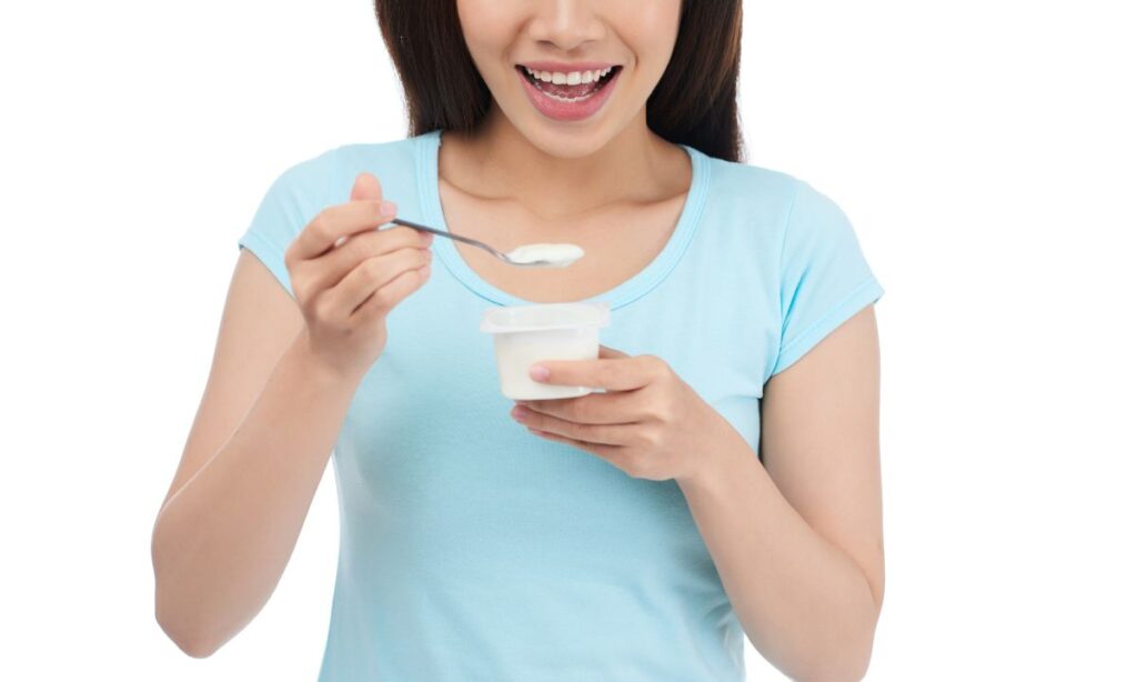 A girl in blue top is eating the yogurt from the cup.