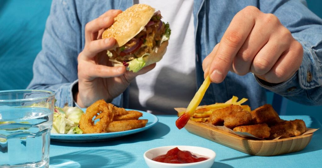 A man's eating unhealthy food, e.g. burger, chips and deep-fried nuggets